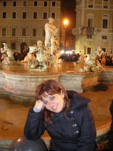 Smiling girl posing in front of the Moor Fountain in Piazza Navona, Rome, at night