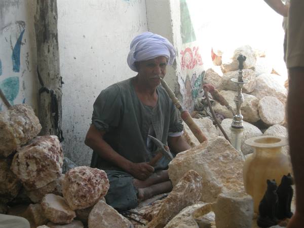 Craftsman in white turban chisels alabaster beside a hookah