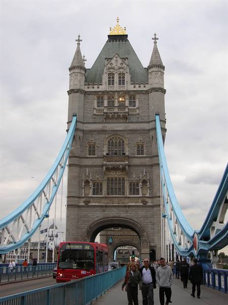 Tourists walk on London's Tower Bridge, a red bus passes beneath the stone tower