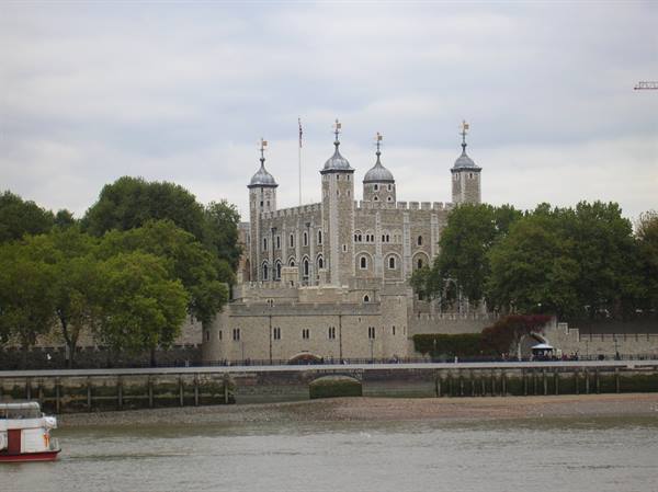 The Tower of London behind trees seen from the Thames with a boat