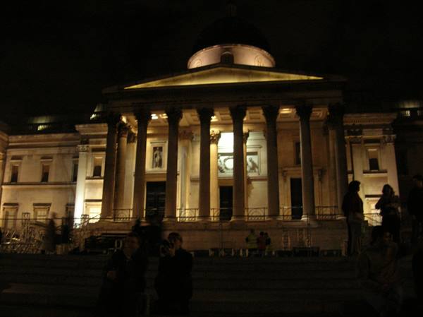 National Gallery in London lit up at night, people sitting on the steps