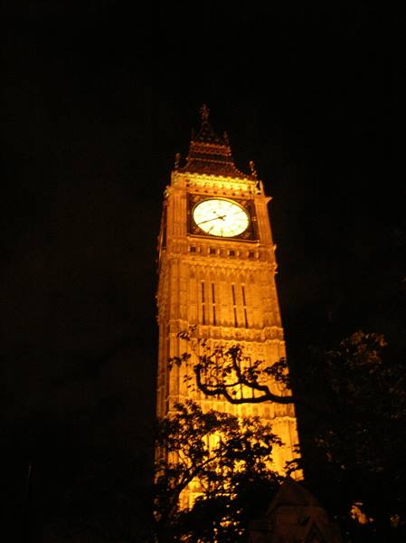 Big Ben lit up at night in London, glowing clock among dark trees