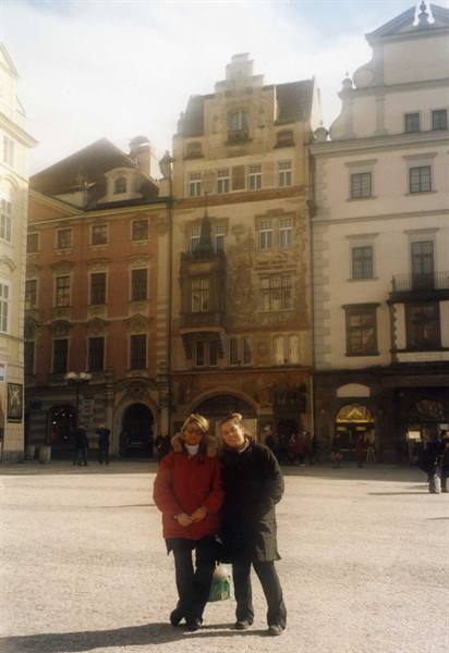 Two women pose on a square in front of the frescoed Helblinghaus in Innsbruck