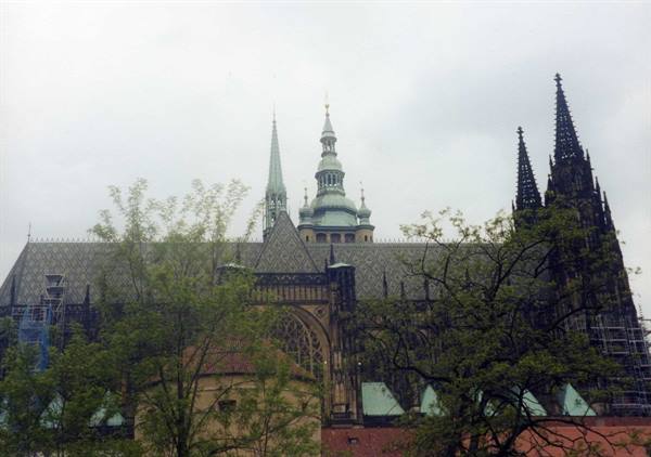 Gothic spires of St. Vitus Cathedral in Prague among green trees, grey sky