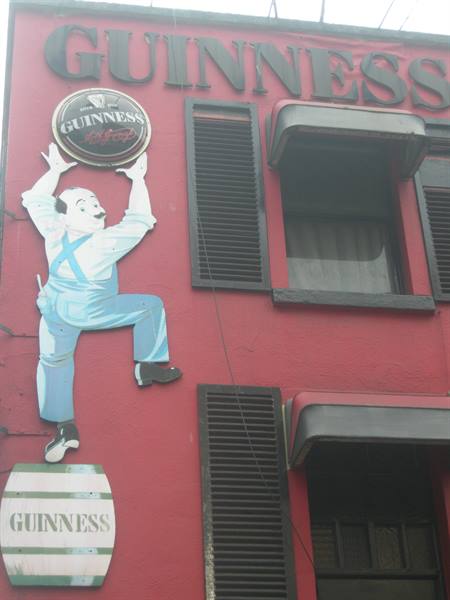 Guinness sign on red facade, figure lifting a barrel
