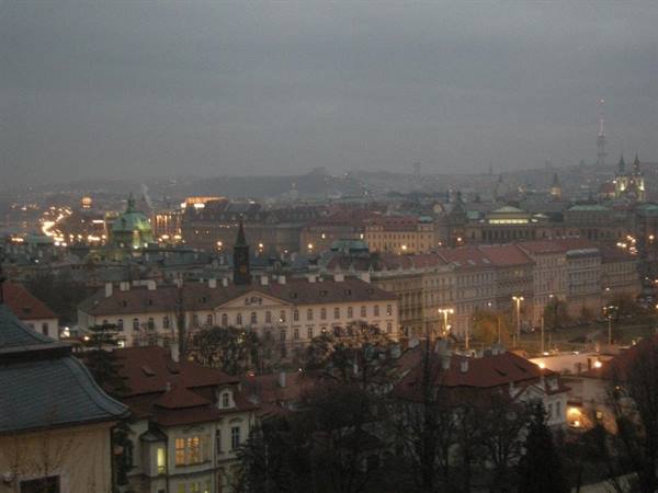 Prague red rooftops under gray sky, city lights glowing