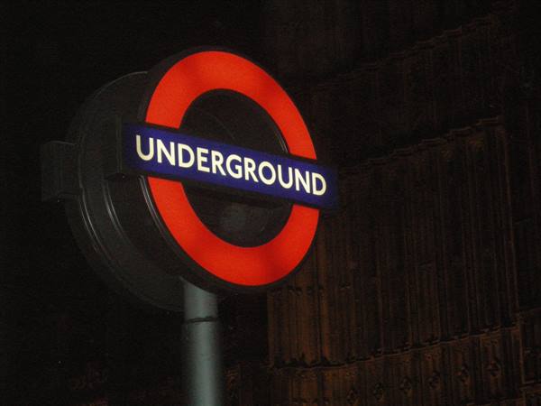 Illuminated red and blue London Underground sign glowing at night