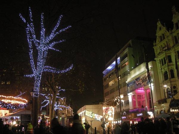 Tree wrapped in blue lights at Leicester Square, London, night crowd below