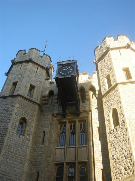 Black clock on the crenellated Tower of London towers, pale stone under sun