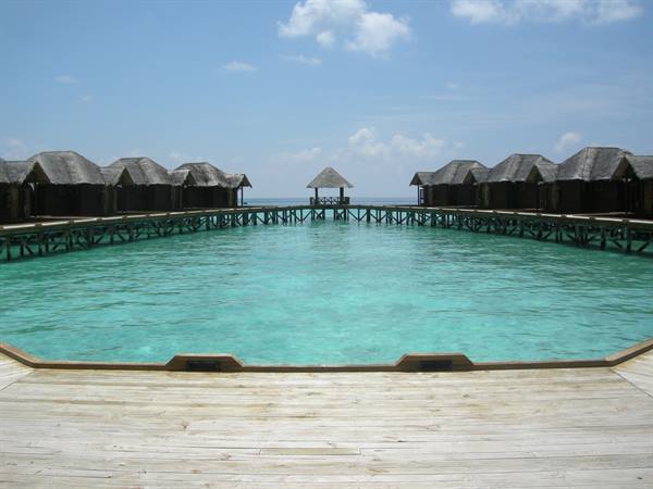 Overwater bungalows on stilts above turquoise water, wooden walkways and central pavilion