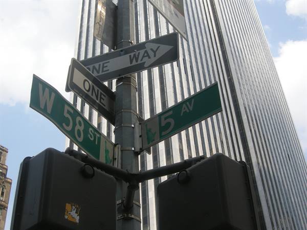 W 58 St and 5 Av street signs on metal pole, glass skyscraper behind
