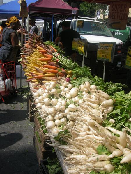 Market stall with white radishes and rainbow carrots under canopies