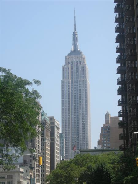 The Empire State Building rises between Manhattan buildings and green trees