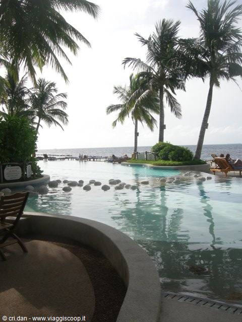 Pool with white stones among palms and wooden loungers by the sea