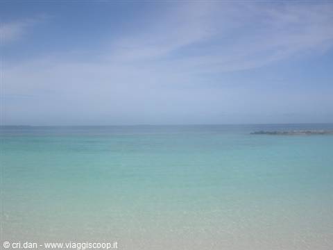 Clear turquoise water over pale sand, dark rocks on the right