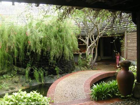 Courtyard with curved stone path, terracotta vases and lush plants under wooden roof