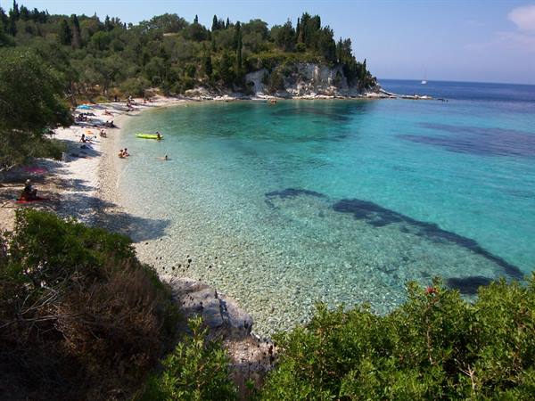 Antipaxos beach, white pebbles under turquoise water, swimmers and kayakers among pines