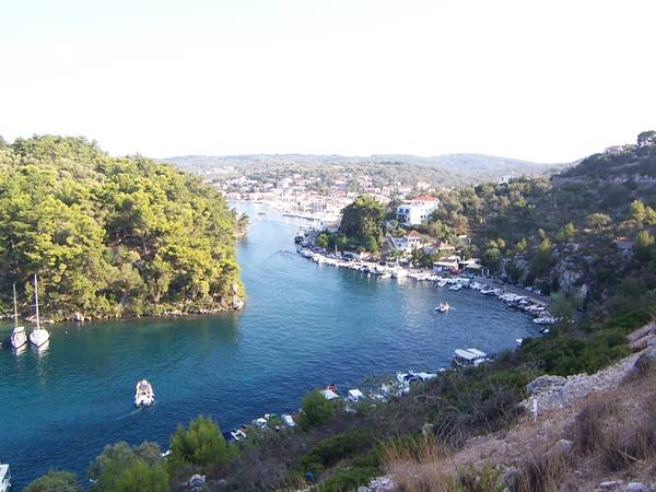 Boat sails between wooded shores toward Paxos harbor, turquoise water