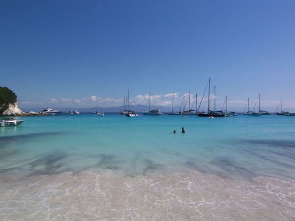 Swimmers in turquoise water among anchored sailboats and yachts
