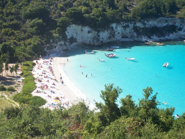 Beachgoers on white sand and boats in turquoise water at Vrika beach, Antipaxos