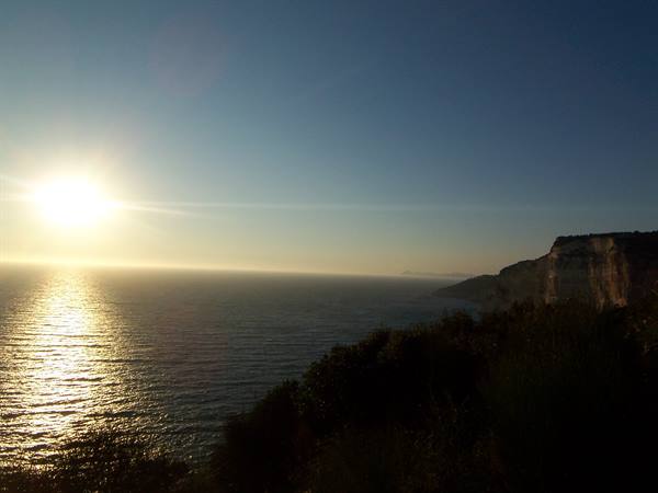 Low sun over the sea, rocky cliffs on the right, backlit vegetation
