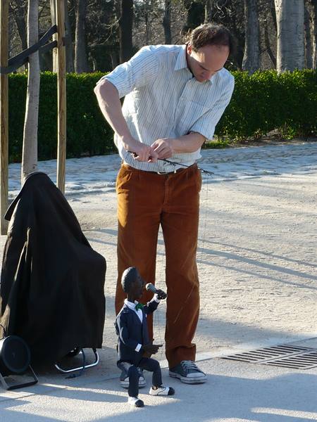 Puppeteer operating a tuxedo puppet singing into a microphone in a park
