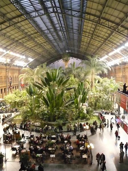 Tropical garden under Madrid Atocha's iron roof, travelers at the café