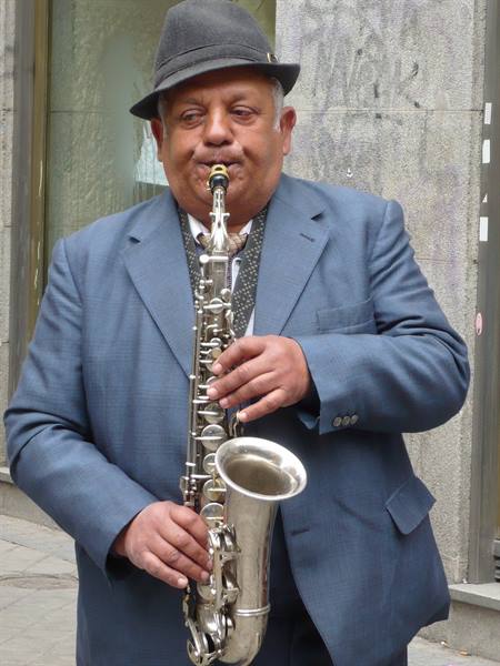 Man in gray hat and blue jacket playing saxophone on the street