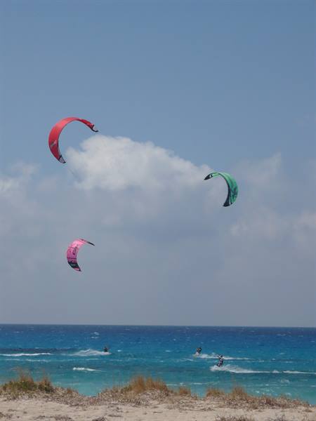 Three colorful kitesurf kites over turquoise sea with sandy dunes