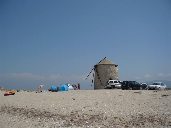 Old stone windmill on the beach, with tents and parked cars
