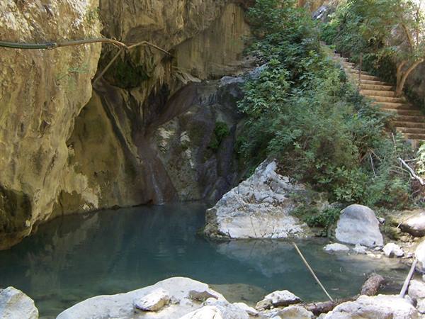 Spring trickling over limestone rock, turquoise pool and stone steps in the bushes