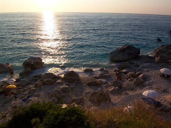 Rocky beach with umbrellas under low sun on the sea