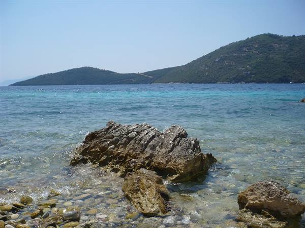 Rock in clear turquoise water, green hills in background, pebbles in foreground