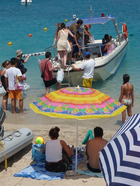 Tourists board a white motorboat from the beach with colorful striped umbrellas