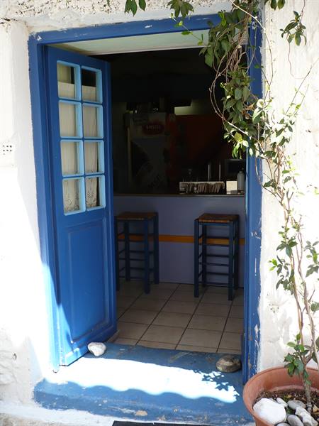 Open blue door leading to a small bar with wooden stools, white wall
