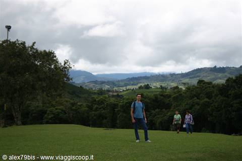 Tourists walking on green lawn under grey clouds, cultivated hills behind