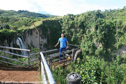 Tourist on wooden platform in front of waterfall between green cliffs