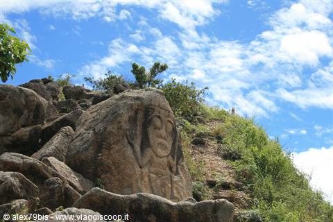 Ancient petroglyph carved into boulder among greenery and cloudy sky