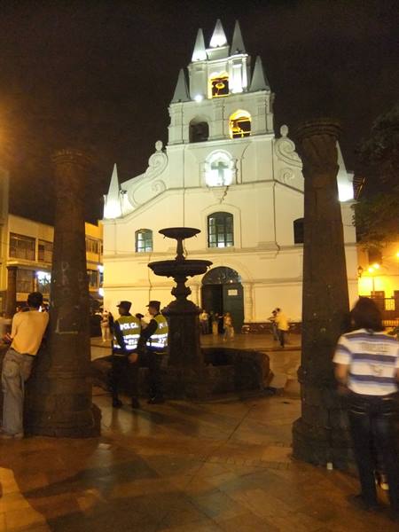 White church lit at night with stone fountain and police officers on the square
