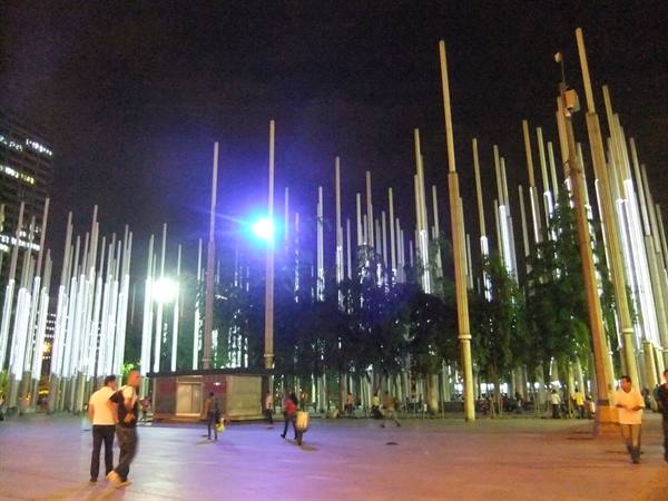 Plaza Cisneros in Medellín: illuminated light towers, people strolling at night
