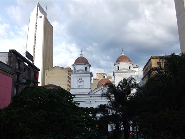 White church with two terracotta domes among palm trees and skyscrapers under cloudy sky