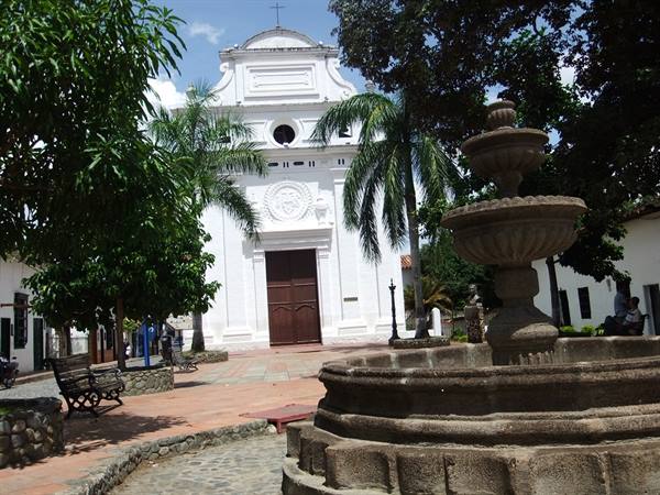 White colonial church with wooden door, stone fountain and palms on the square