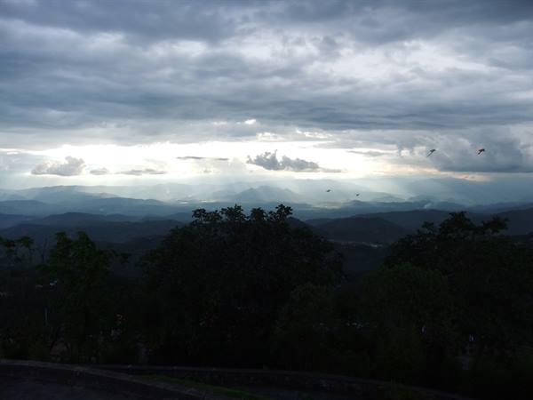Dark clouds over blue mountains, green trees, birds flying