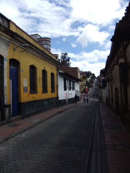 Cobbled uphill street between yellow and white colonial houses, La Candelaria, Bogotá