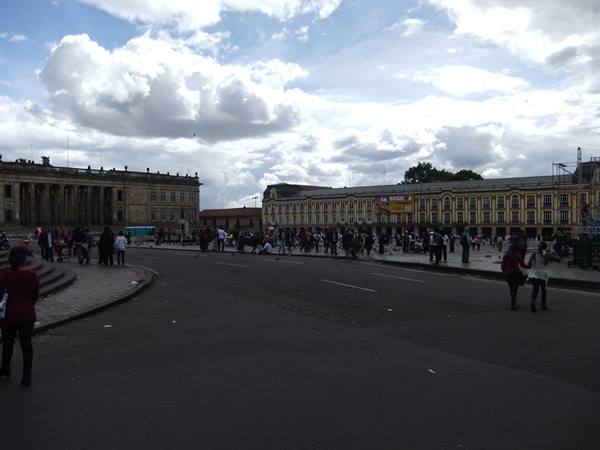People stroll through Plaza de Bolívar among colonial buildings under white clouds