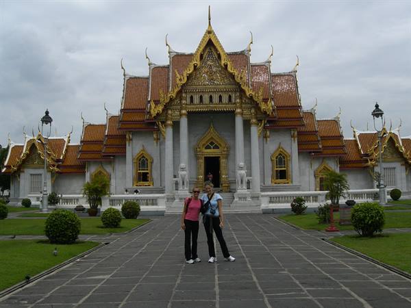 Two tourists pose in front of Wat Benchamabophit, white marble temple in Bangkok