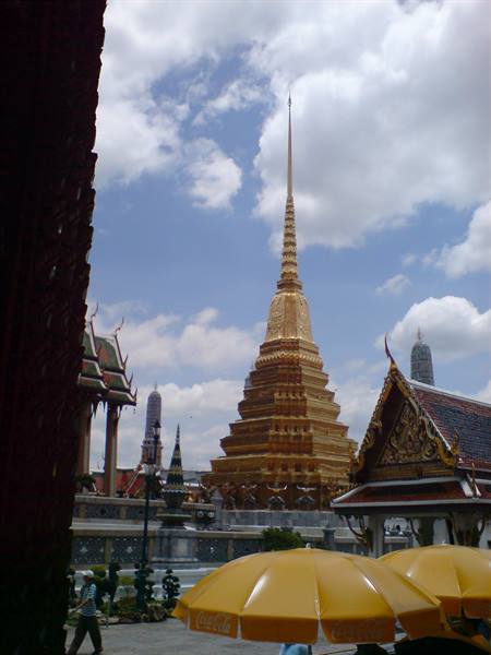 Golden stupa at Wat Phra Kaew, yellow umbrellas and tourists under a cloudy sky