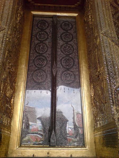 Gilded temple door with carved medallions reflecting the rooftops of Wat Phra Kaew