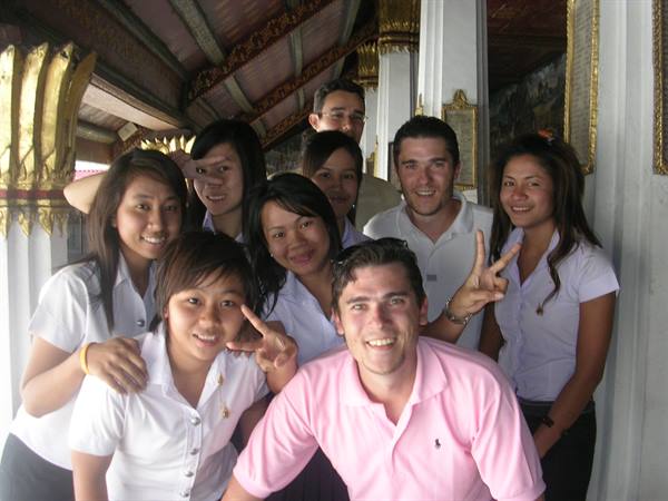 Tourists and students in white shirts smiling under a golden temple roof