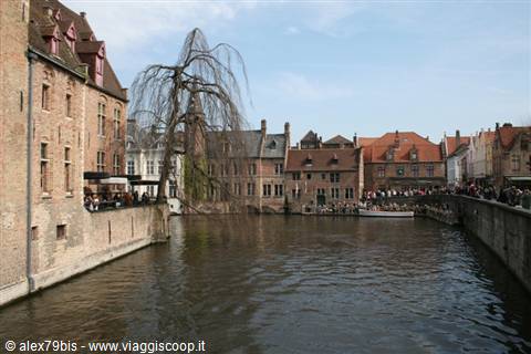 Bruges canal flanked by brick houses, weeping willow and crowds on walls